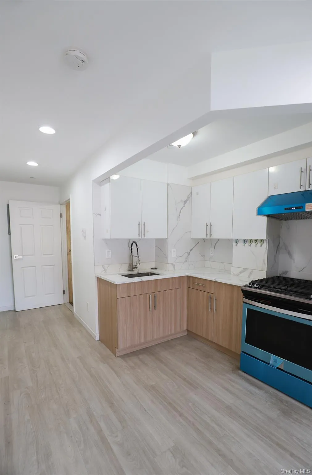 Kitchen featuring tasteful backsplash, range with gas cooktop, white cabinets, light wood-style flooring, and light brown cabinets Kitchen featuring tasteful backsplash, range with gas cooktop, white cabinets, light wood-style flooring, and light brown cabinets