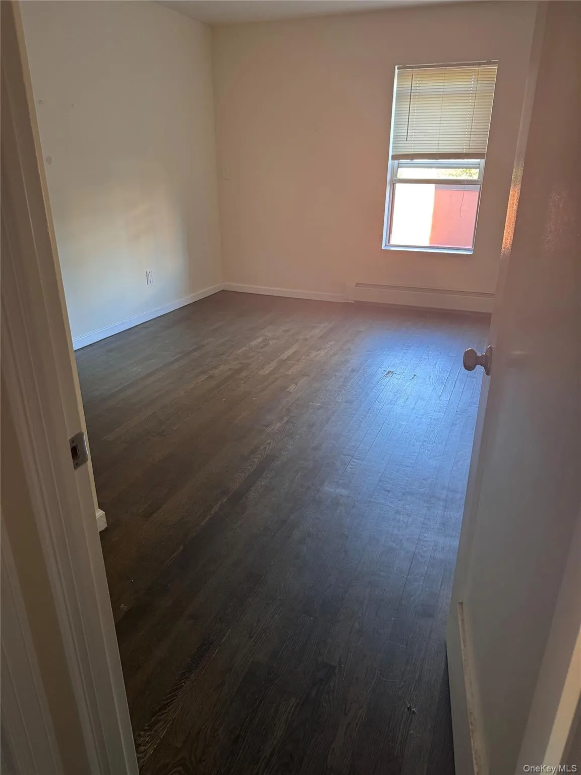 Unfurnished room featuring dark wood-style flooring and a baseboard heating unit Unfurnished room featuring dark wood-style flooring and a baseboard heating unit