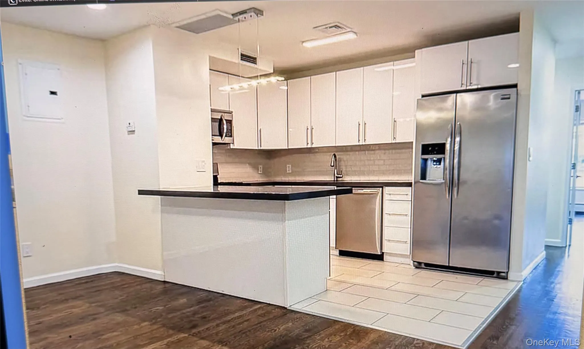 Kitchen featuring appliances with stainless steel finishes, a peninsula, decorative backsplash, dark countertops, and hanging light fixtures Kitchen featuring appliances with stainless steel finishes, a peninsula, decorative backsplash, dark countertops, and hanging light fixtures
