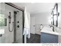 Full bathroom with double vanity, a stall shower, tile walls, and a wainscoted wall Full bathroom with double vanity, a stall shower, tile walls, and a wainscoted wall
