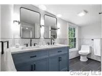 Full bathroom with double vanity, dark tile patterned flooring, tile walls, and wainscoting Full bathroom with double vanity, dark tile patterned flooring, tile walls, and wainscoting
