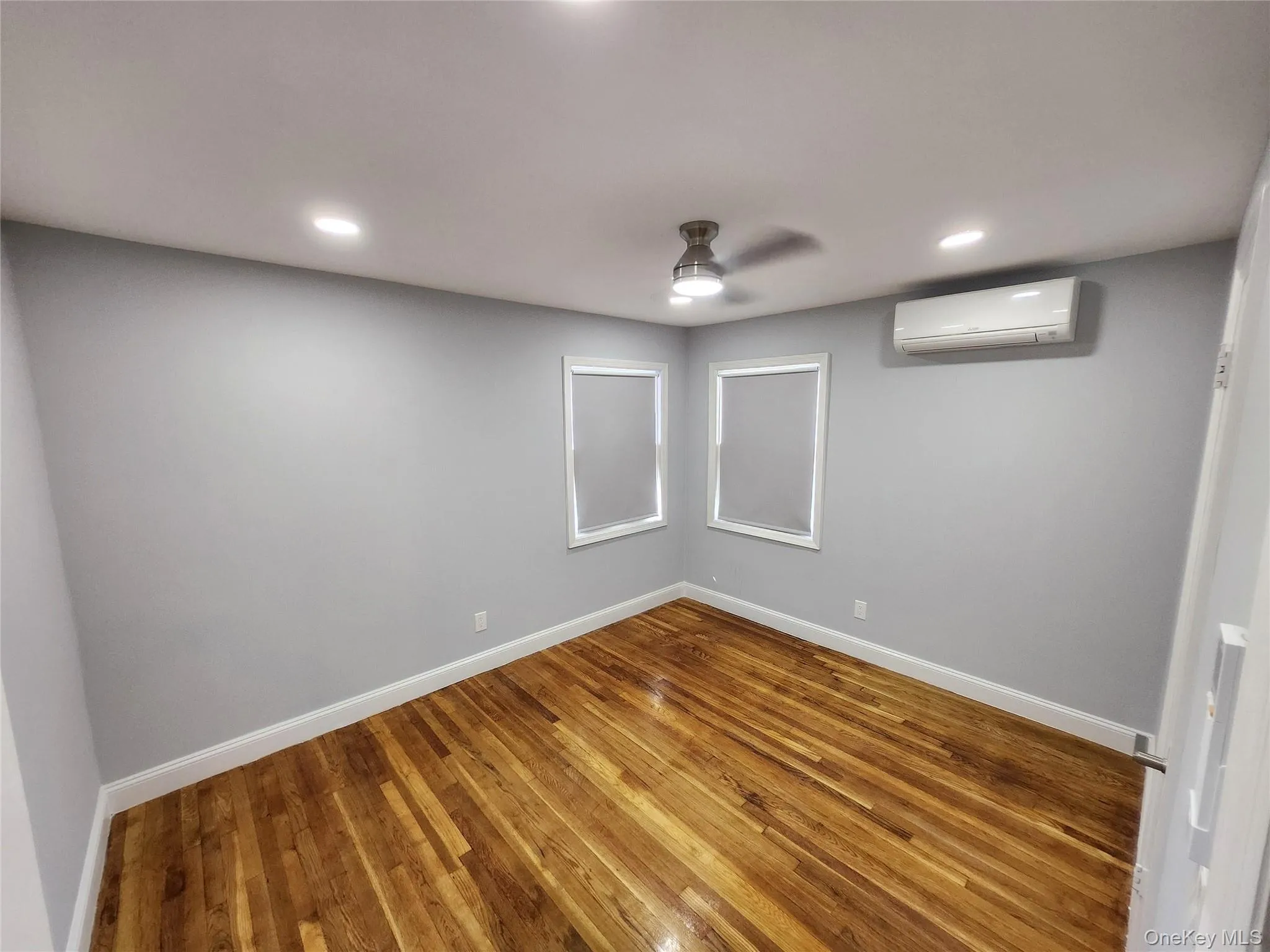 Basement featuring a ceiling fan, baseboards, a wall mounted air conditioner, and wood finished floors Basement featuring a ceiling fan, baseboards, a wall mounted air conditioner, and wood finished floors
