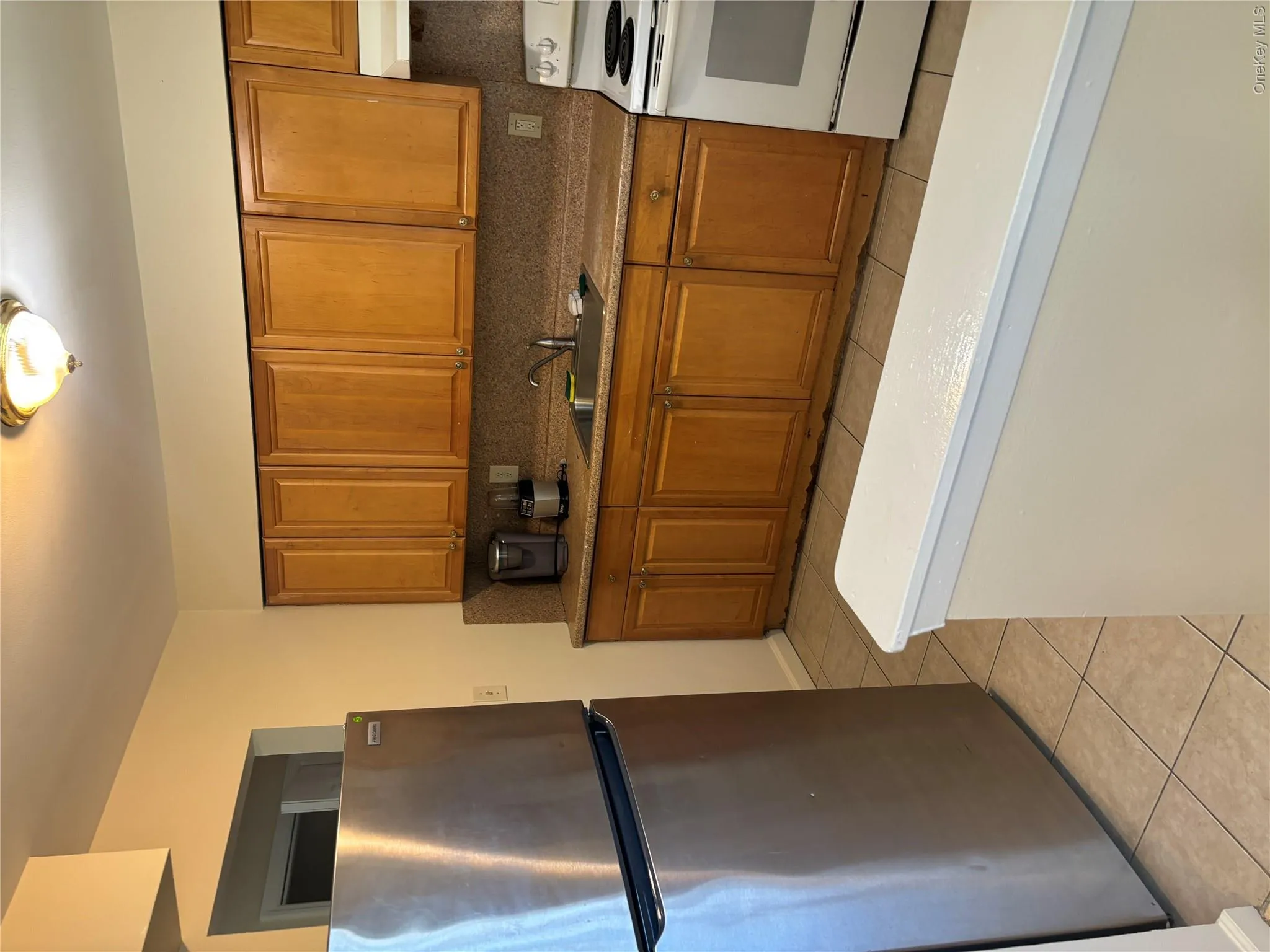 Kitchen featuring stainless steel fridge, tasteful backsplash, brown cabinets, stove, and light tile patterned flooring Kitchen featuring stainless steel fridge, tasteful backsplash, brown cabinets, stove, and light tile patterned flooring