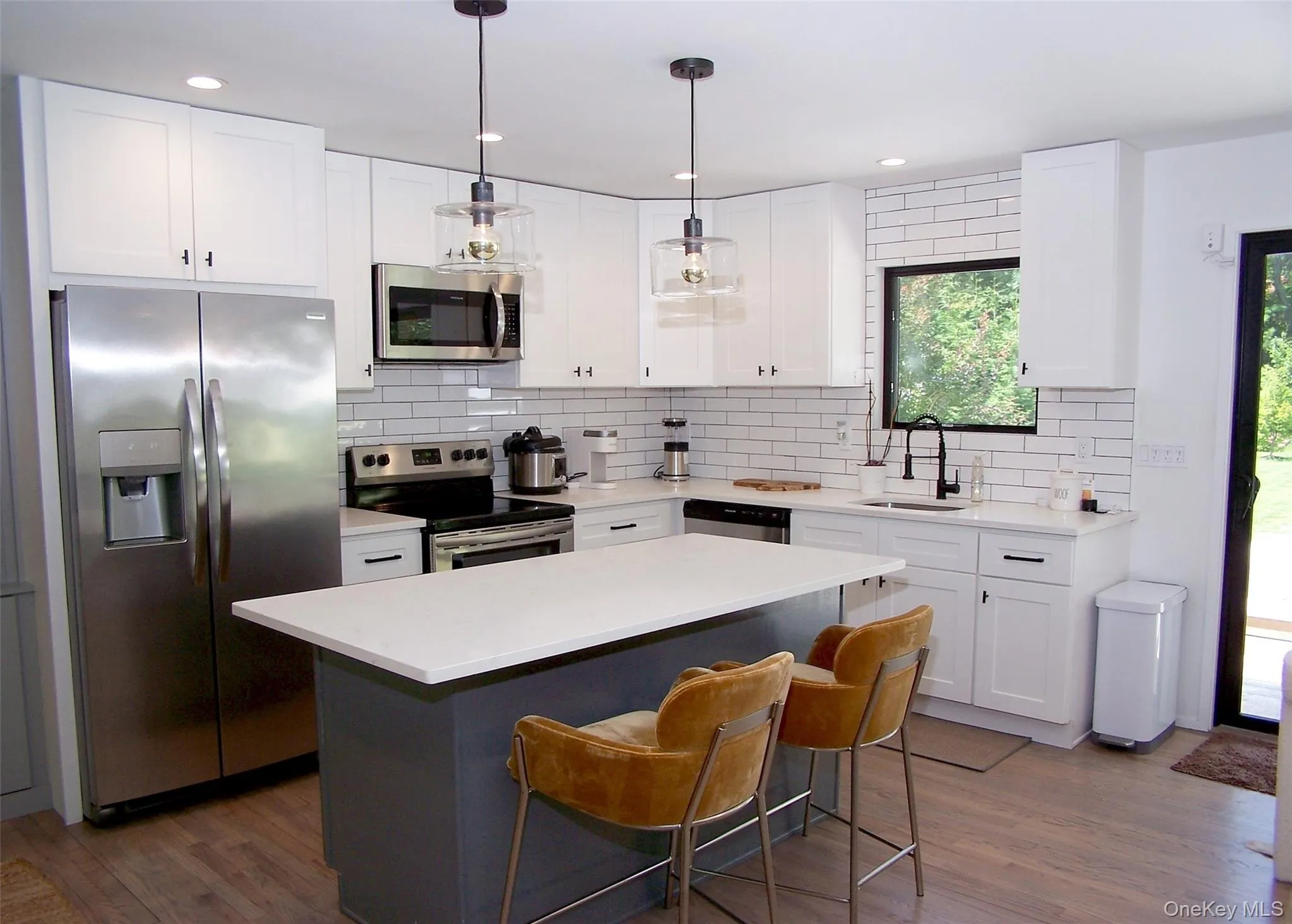 Kitchen with appliances with stainless steel finishes, backsplash, white cabinetry, a kitchen island, and hanging light fixtures Kitchen with appliances with stainless steel finishes, backsplash, white cabinetry, a kitchen island, and hanging light fixtures