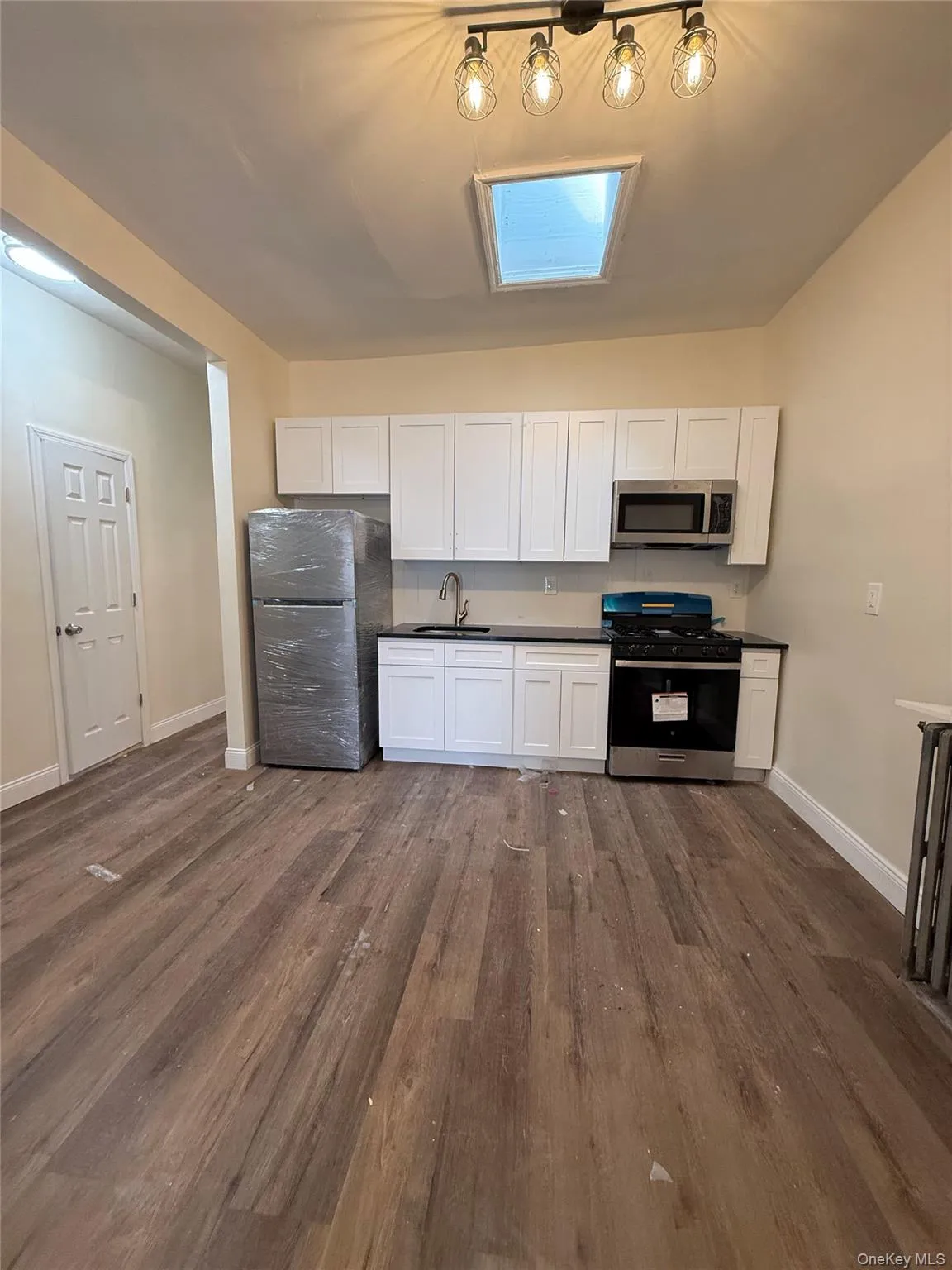 Kitchen featuring white cabinetry, appliances with stainless steel finishes, dark wood-style flooring, dark countertops, and a skylight Kitchen featuring white cabinetry, appliances with stainless steel finishes, dark wood-style flooring, dark countertops, and a skylight