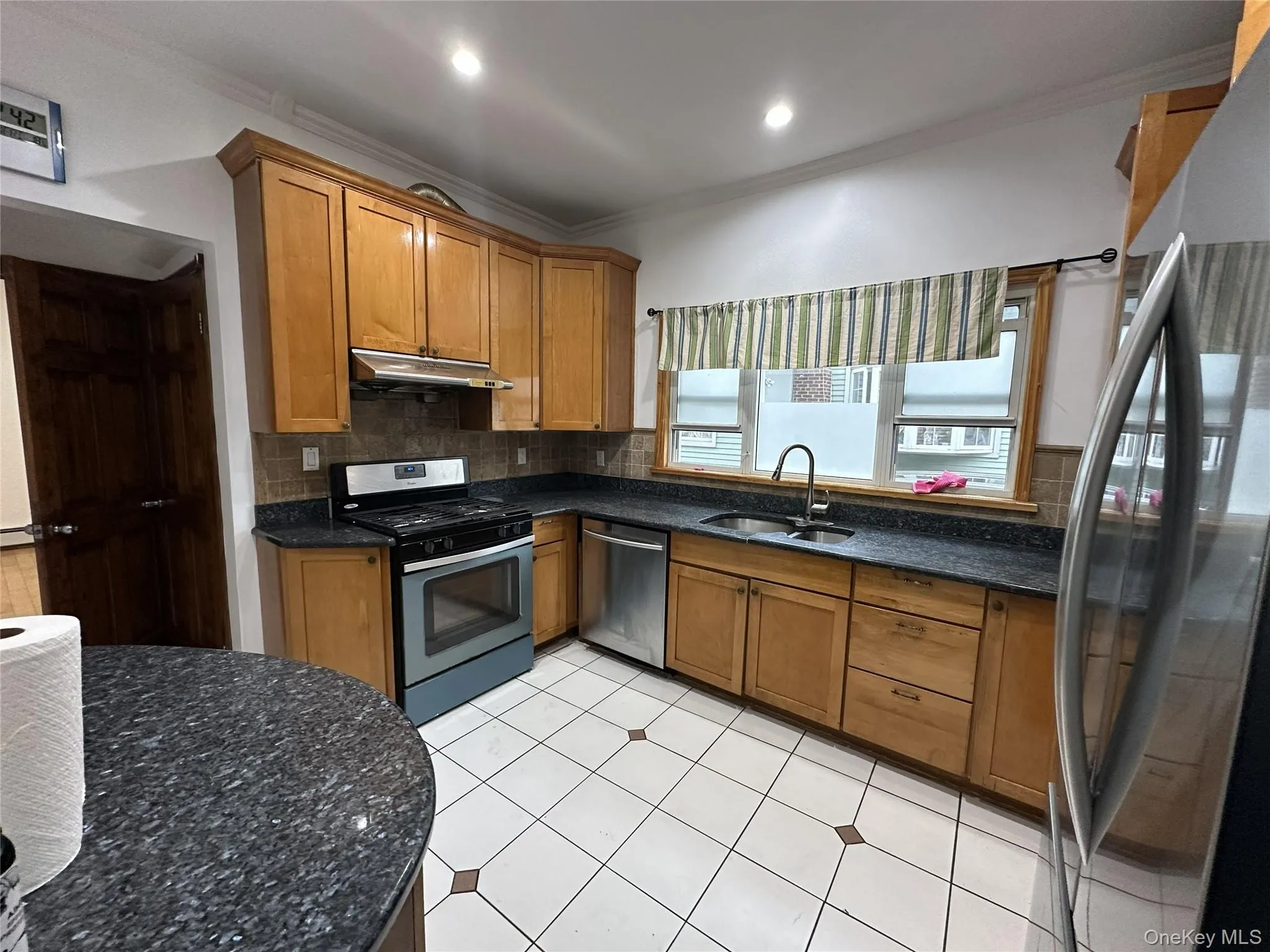 Kitchen featuring brown cabinets, stainless steel appliances, crown molding, decorative backsplash, and dark stone counters Kitchen featuring brown cabinets, stainless steel appliances, crown molding, decorative backsplash, and dark stone counters