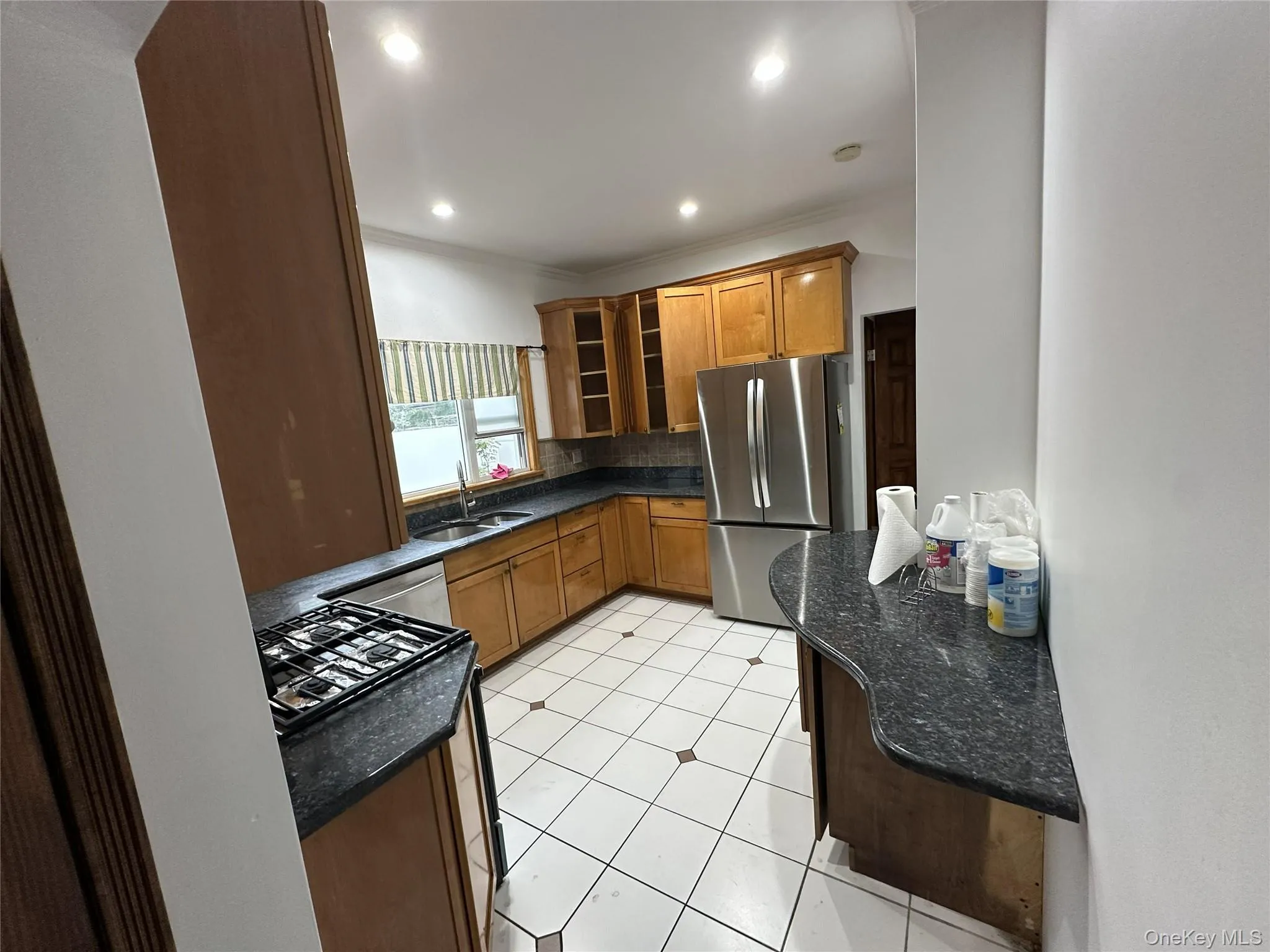 Kitchen featuring stainless steel appliances, backsplash, glass insert cabinets, dark stone countertops, and brown cabinetry Kitchen featuring stainless steel appliances, backsplash, glass insert cabinets, dark stone countertops, and brown cabinetry