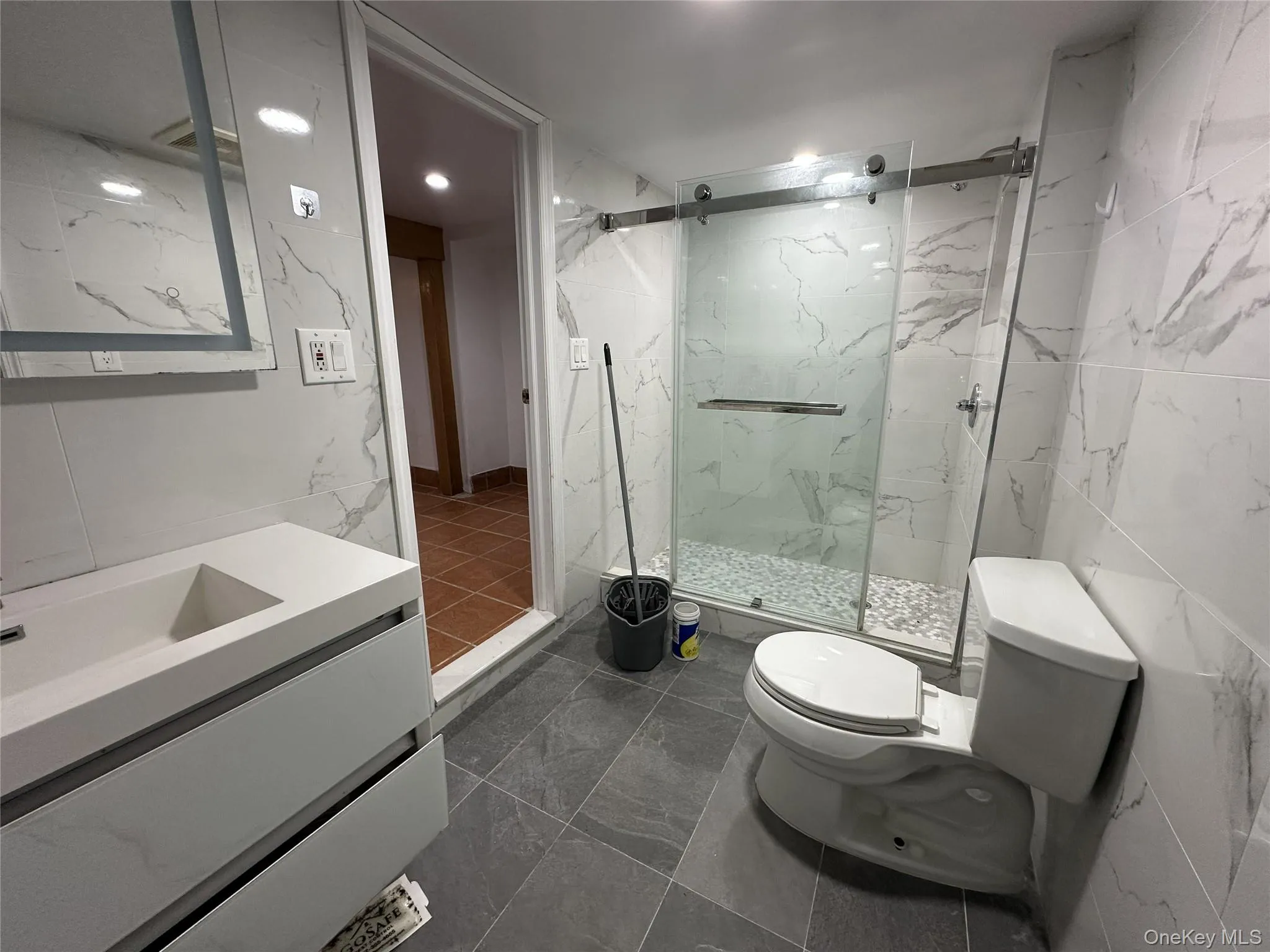Bathroom featuring tile walls, vanity, a marble finish shower, and dark marble finish floors Bathroom featuring tile walls, vanity, a marble finish shower, and dark marble finish floors