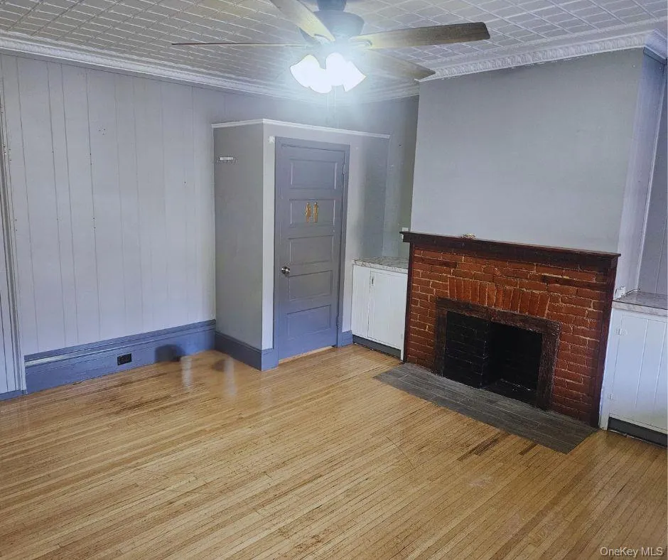 Unfurnished room with light wood-style floors, a fireplace, wooden walls, ceiling fan, and crown molding Unfurnished room with light wood-style floors, a fireplace, wooden walls, ceiling fan, and crown molding