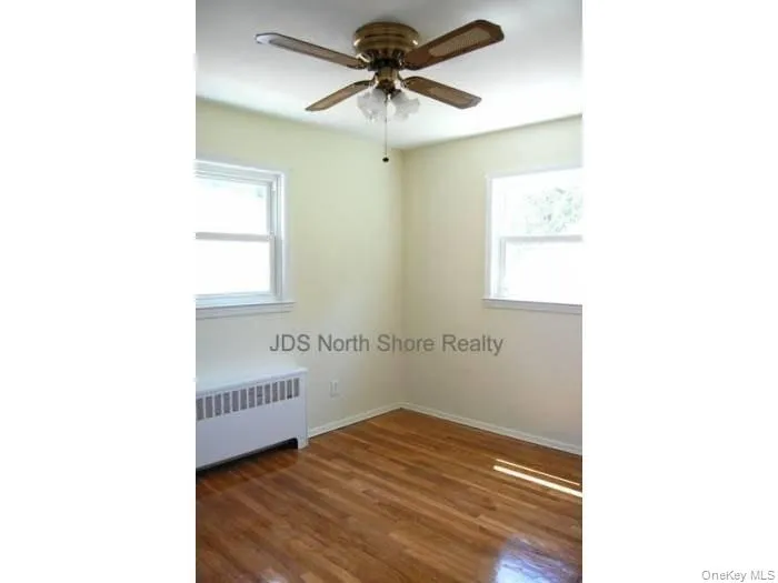 Empty room featuring radiator heating unit, dark wood-type flooring, and a ceiling fan Empty room featuring radiator heating unit, dark wood-type flooring, and a ceiling fan