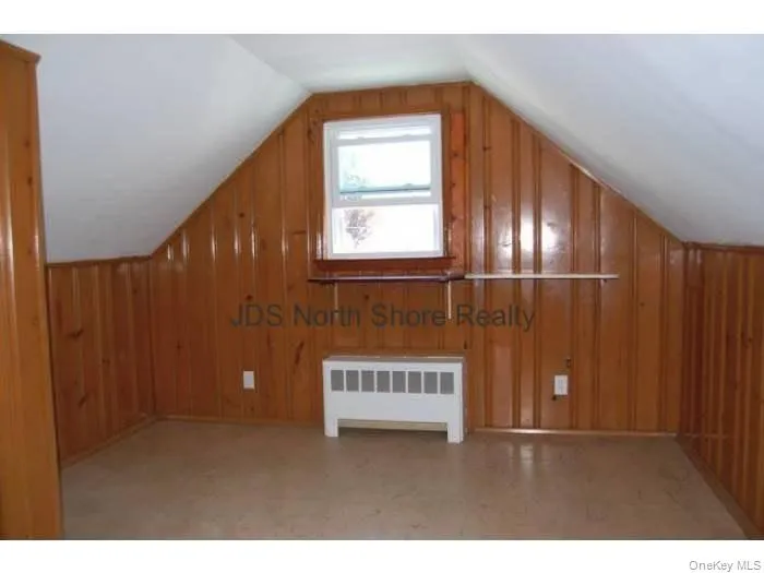 Additional living space featuring wood walls, vaulted ceiling, and radiator Additional living space featuring wood walls, vaulted ceiling, and radiator
