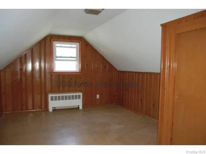 Additional living space featuring wooden walls, lofted ceiling, and radiator Additional living space featuring wooden walls, lofted ceiling, and radiator