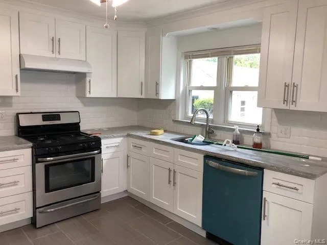 Kitchen with gas range, white cabinets, dishwasher, decorative backsplash, and under cabinet range hood Kitchen with gas range, white cabinets, dishwasher, decorative backsplash, and under cabinet range hood