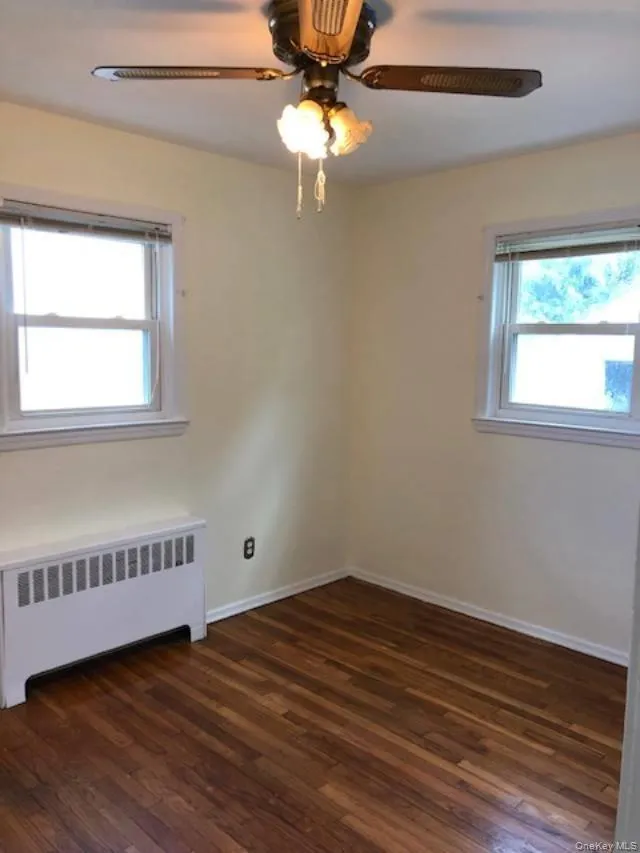 Spare room with radiator, dark wood finished floors, and ceiling fan Spare room with radiator, dark wood finished floors, and ceiling fan