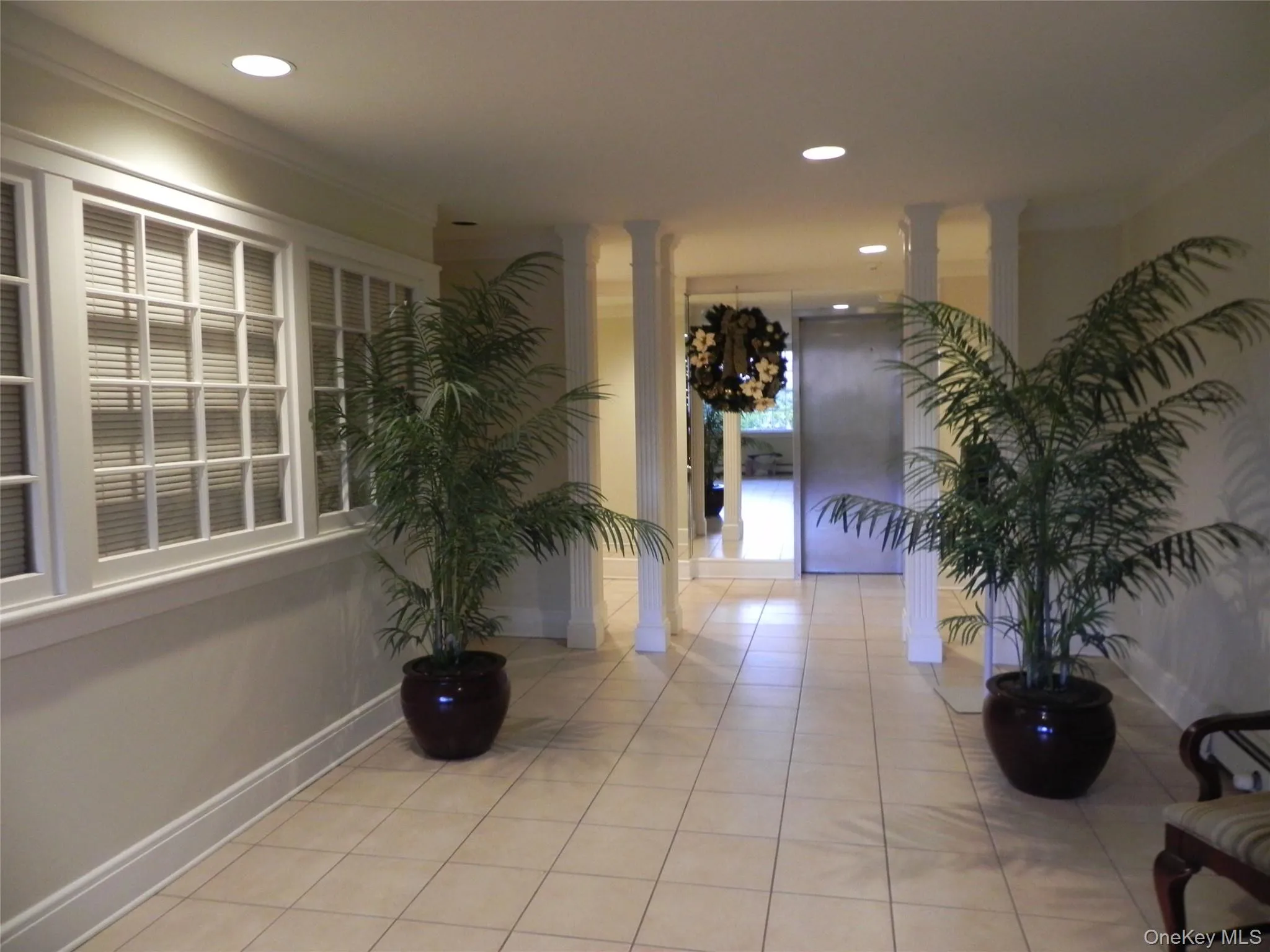 Hallway featuring light tile patterned flooring, crown molding, and decorative columns Hallway featuring light tile patterned flooring, crown molding, and decorative columns