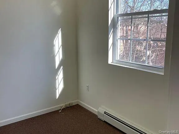 Empty room with a baseboard heating unit and dark carpet Empty room with a baseboard heating unit and dark carpet