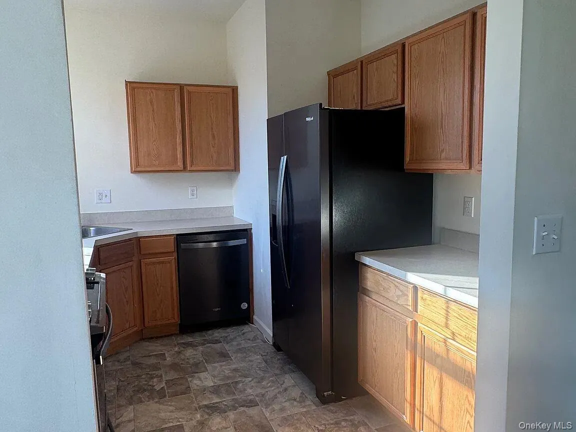 Kitchen with dishwashing machine, brown cabinets, light countertops, and black fridge with ice dispenser Kitchen with dishwashing machine, brown cabinets, light countertops, and black fridge with ice dispenser