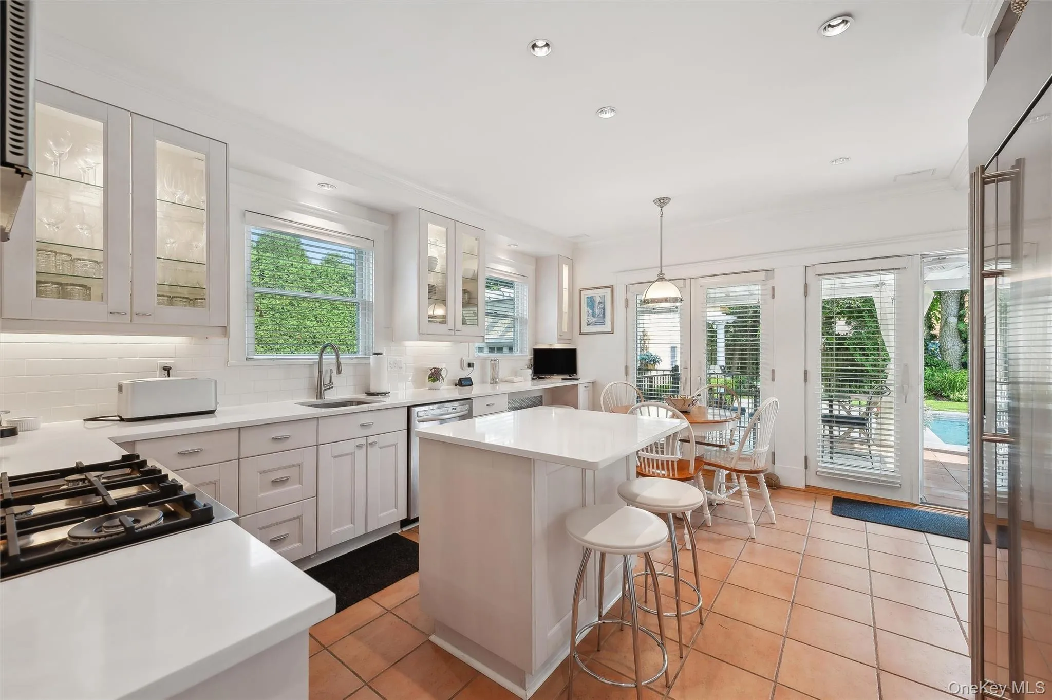 Kitchen with pendant lighting, a kitchen breakfast bar, light tile patterned flooring, tasteful backsplash, and white cabinetry Kitchen with pendant lighting, a kitchen breakfast bar, light tile patterned flooring, tasteful backsplash, and white cabinetry