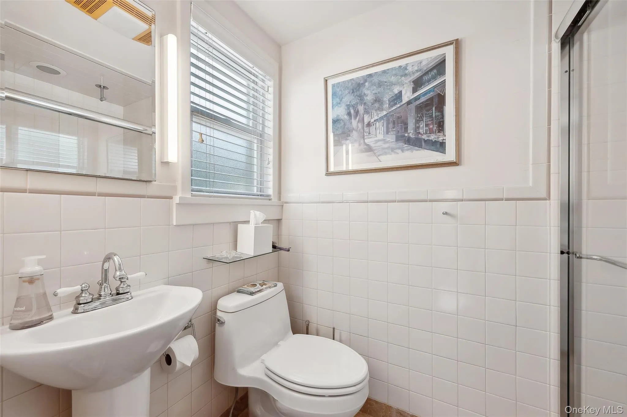 Bathroom with tile walls, a shower stall, and a wainscoted wall Bathroom with tile walls, a shower stall, and a wainscoted wall