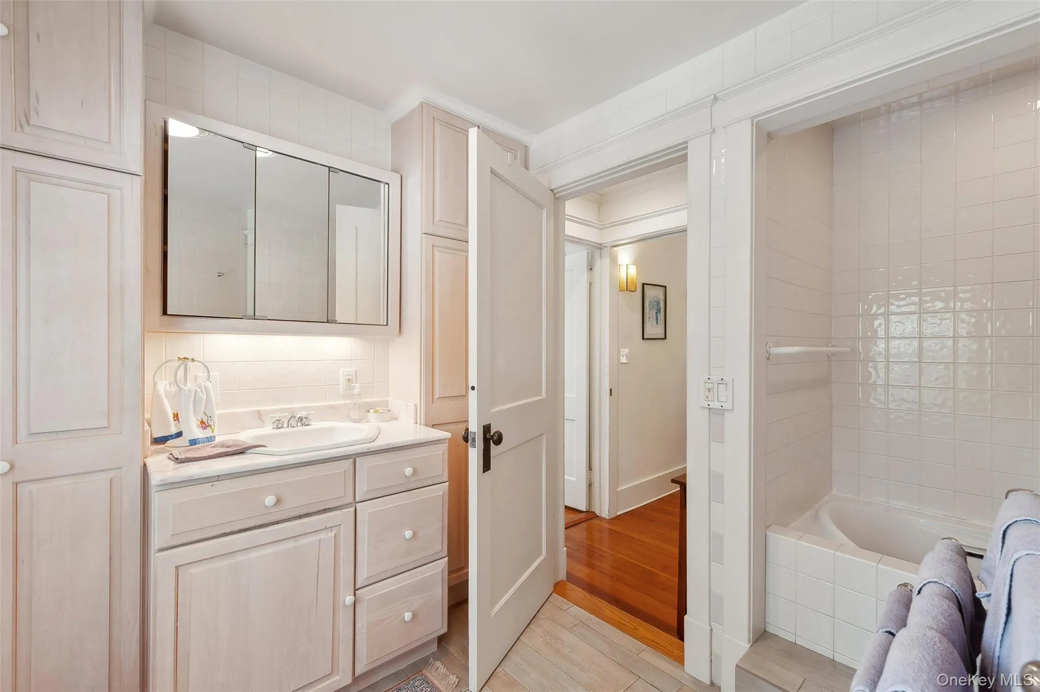 Full bath with vanity, light wood-type flooring, and a relaxing tiled tub Full bath with vanity, light wood-type flooring, and a relaxing tiled tub