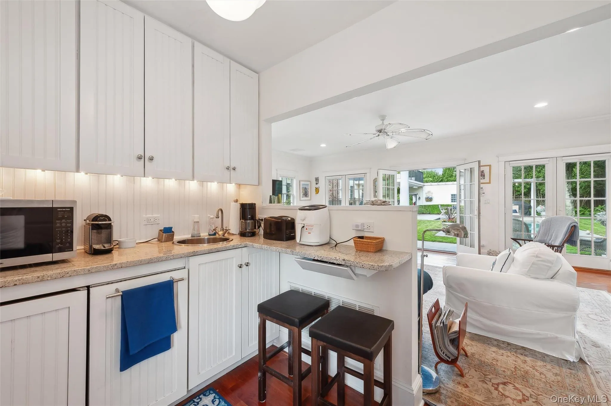 Kitchen with open floor plan, white cabinetry, stainless steel microwave, dark wood-type flooring, and light stone counters Kitchen with open floor plan, white cabinetry, stainless steel microwave, dark wood-type flooring, and light stone counters