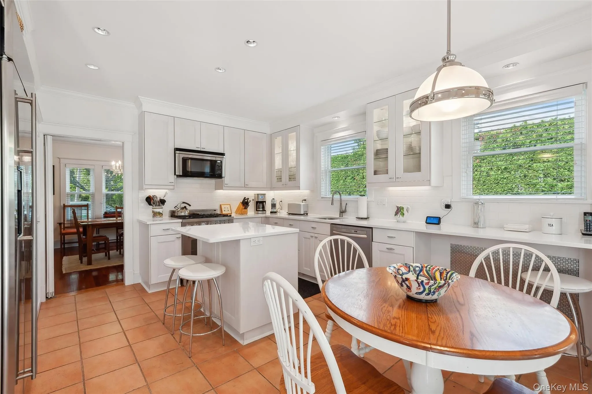 Kitchen featuring glass insert cabinets, tasteful backsplash, hanging light fixtures, white cabinets, and healthy amount of natural light Kitchen featuring glass insert cabinets, tasteful backsplash, hanging light fixtures, white cabinets, and healthy amount of natural light