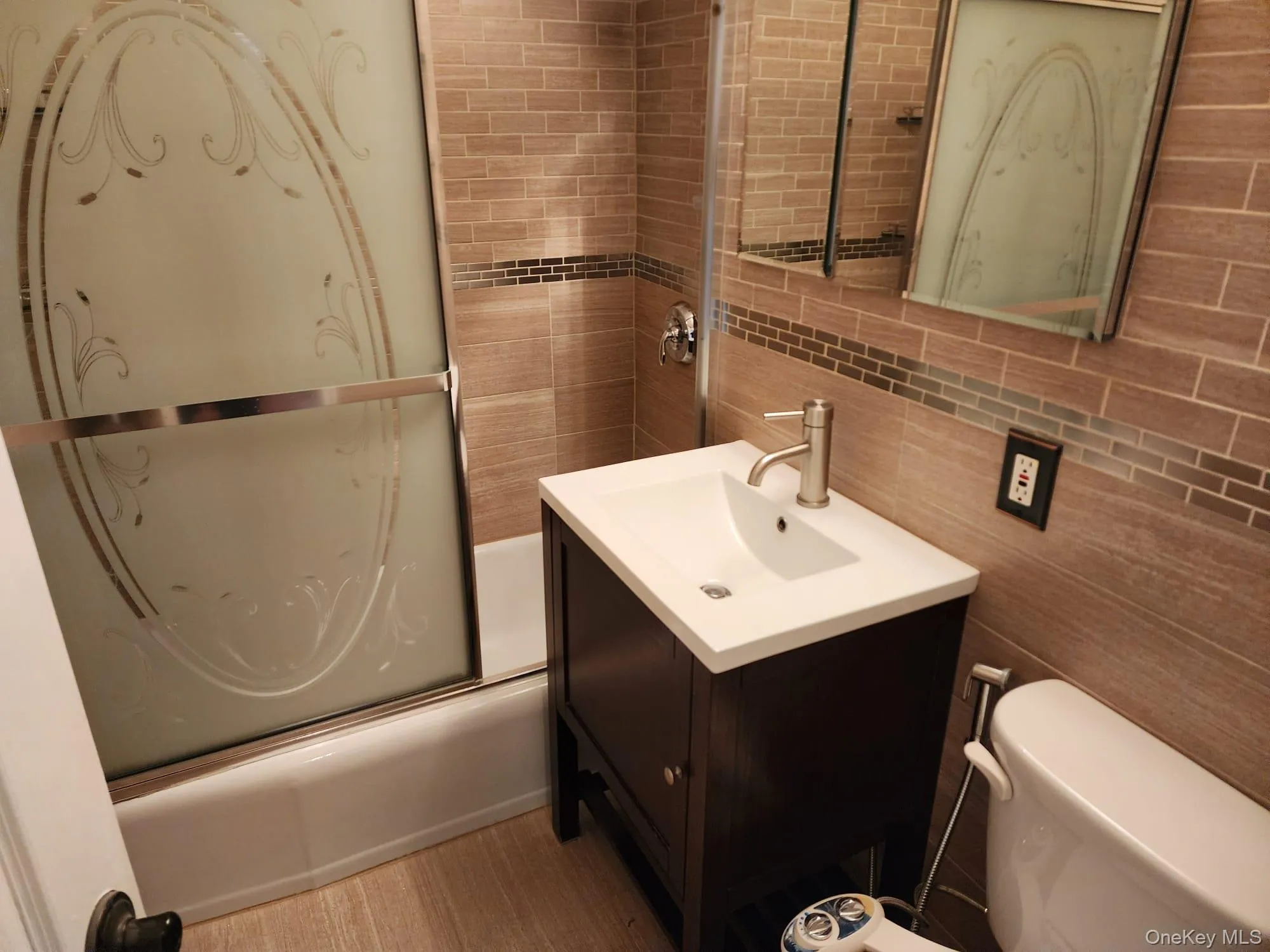 Bathroom featuring tile walls, vanity, shower / bath combination with glass door, and backsplash Bathroom featuring tile walls, vanity, shower / bath combination with glass door, and backsplash