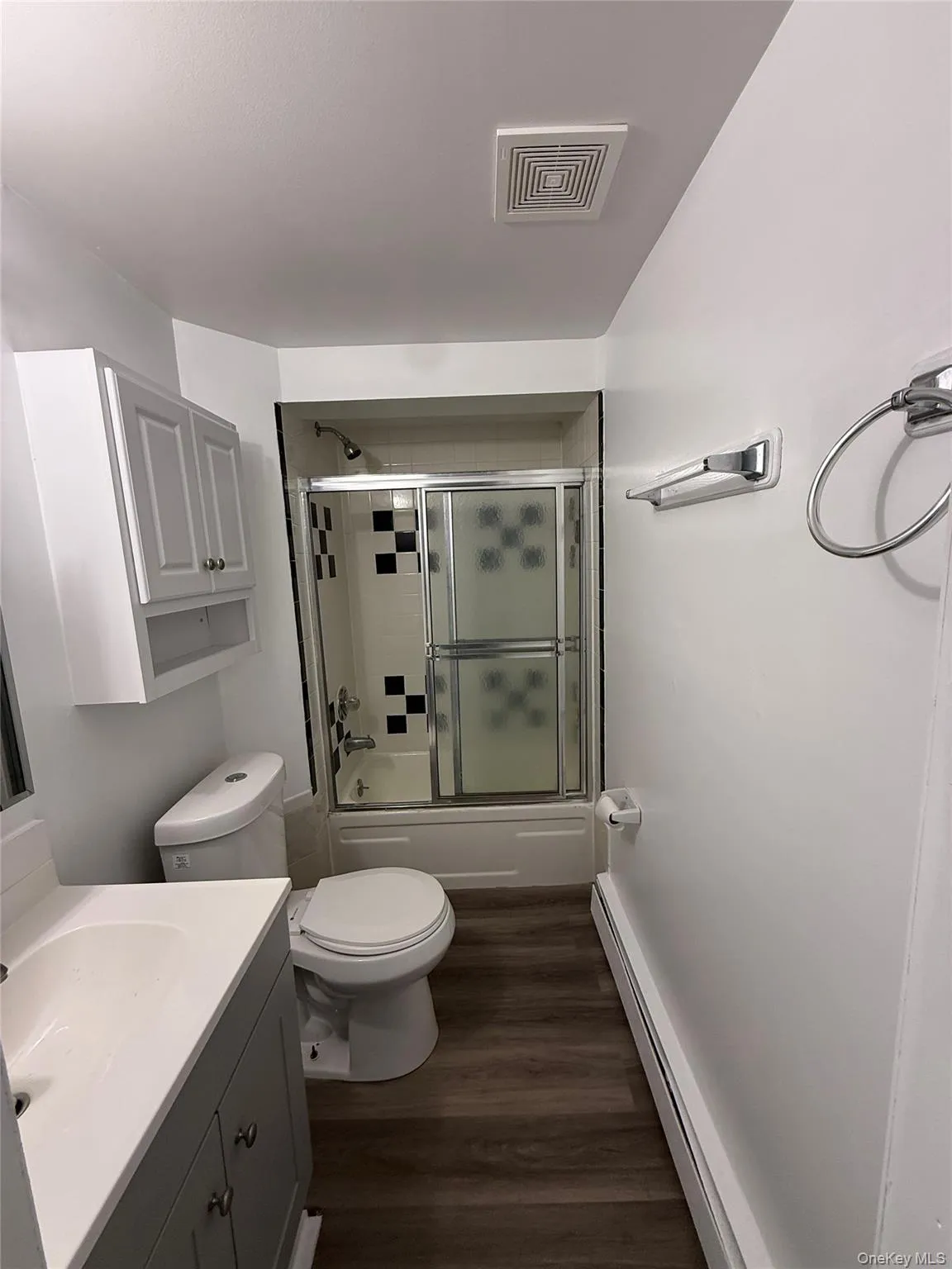 Full bathroom featuring combined bath / shower with glass door, vanity, dark wood-type flooring, and baseboard heating Full bathroom featuring combined bath / shower with glass door, vanity, dark wood-type flooring, and baseboard heating
