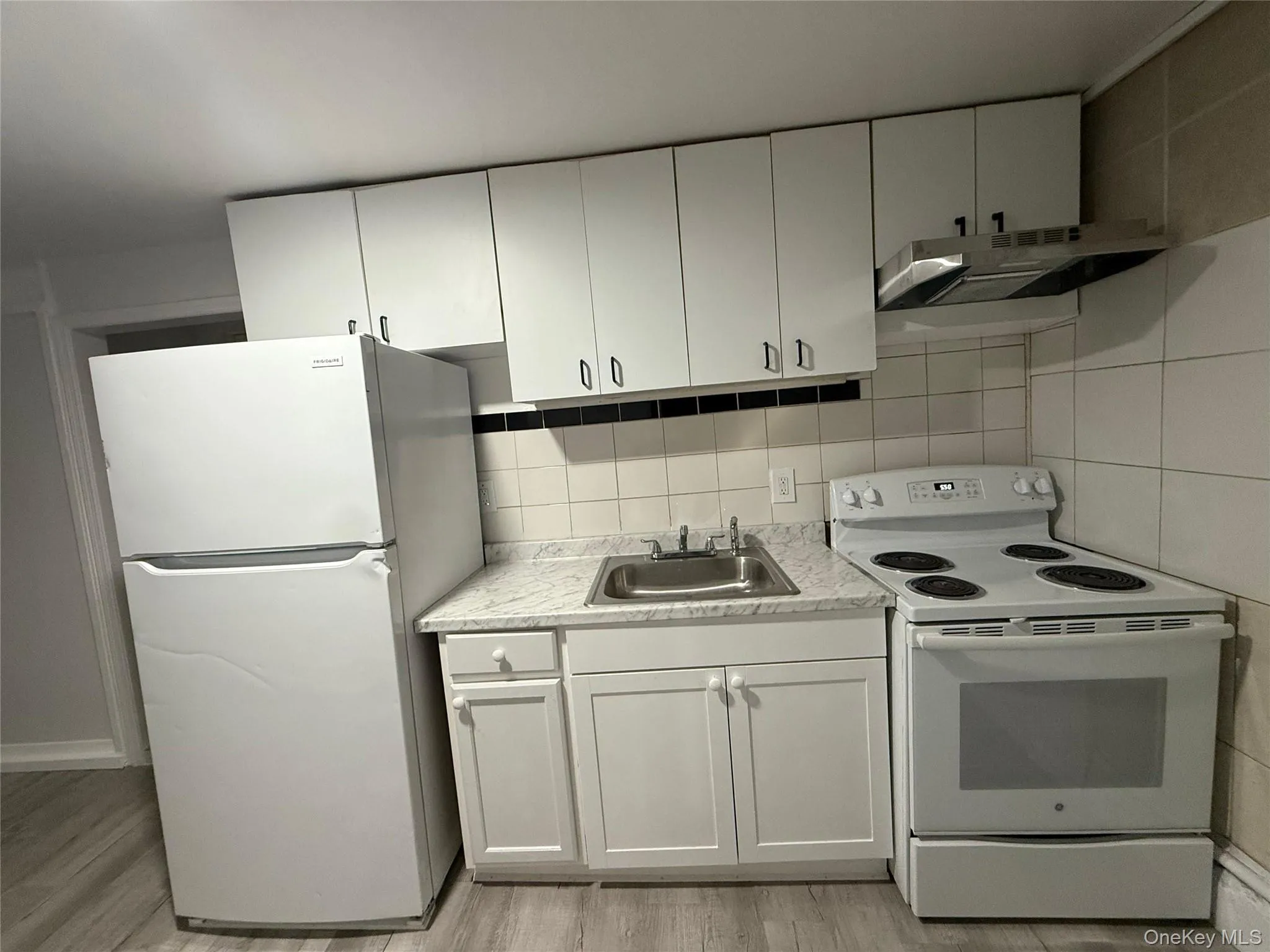 Kitchen featuring white appliances, light countertops, white cabinetry, under cabinet range hood, and light wood finished floors Kitchen featuring white appliances, light countertops, white cabinetry, under cabinet range hood, and light wood finished floors