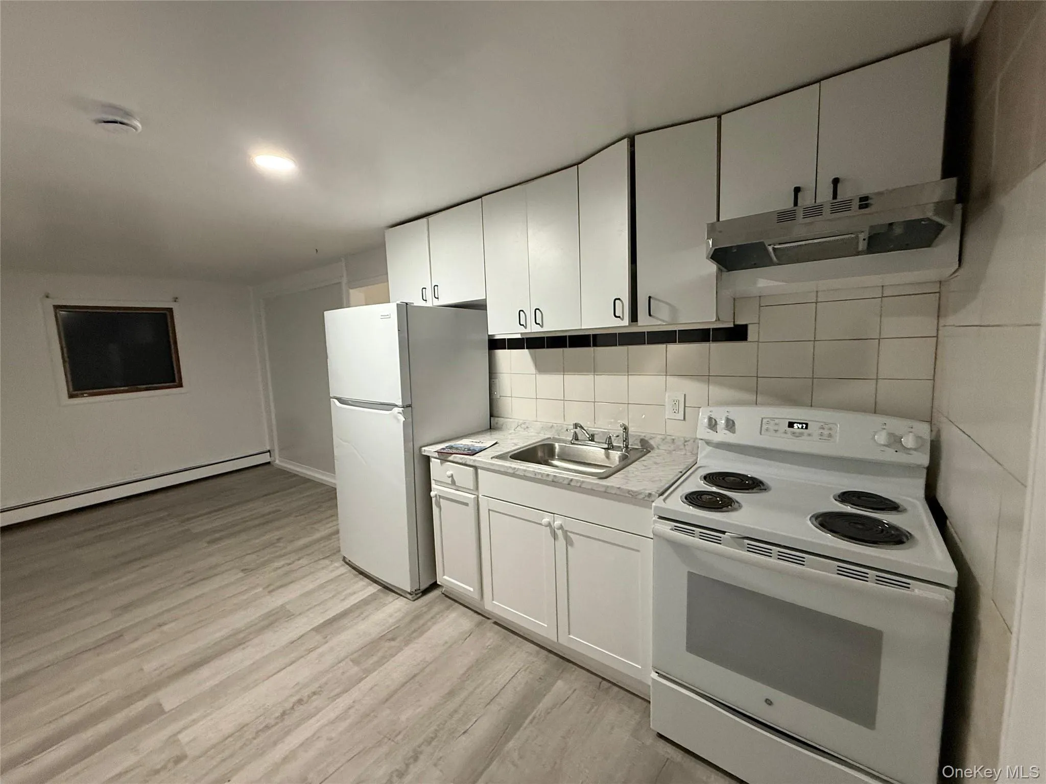 Kitchen featuring white appliances, baseboard heating, under cabinet range hood, light wood-style floors, and light countertops Kitchen featuring white appliances, baseboard heating, under cabinet range hood, light wood-style floors, and light countertops