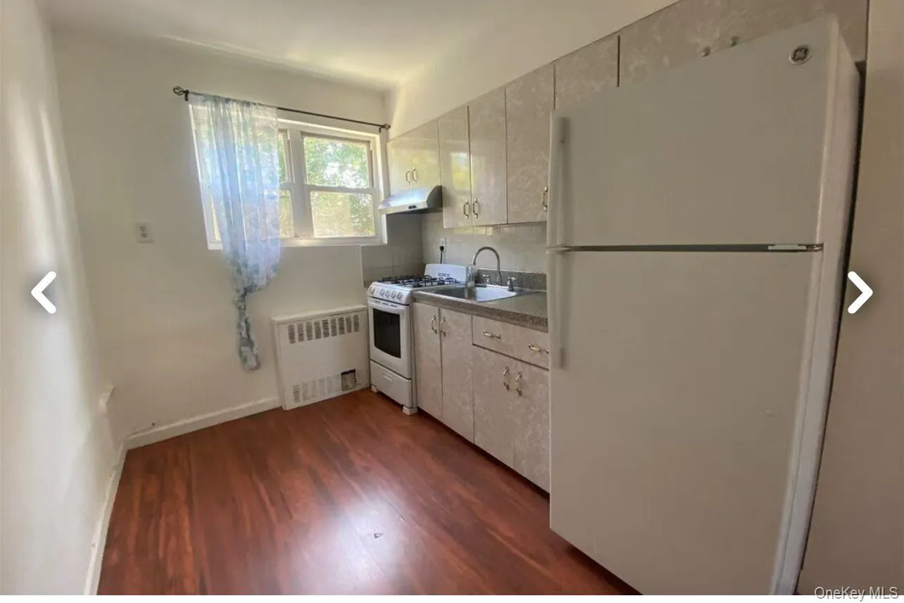 Kitchen with white appliances, radiator heating unit, dark wood-type flooring, and white cabinets Kitchen with white appliances, radiator heating unit, dark wood-type flooring, and white cabinets