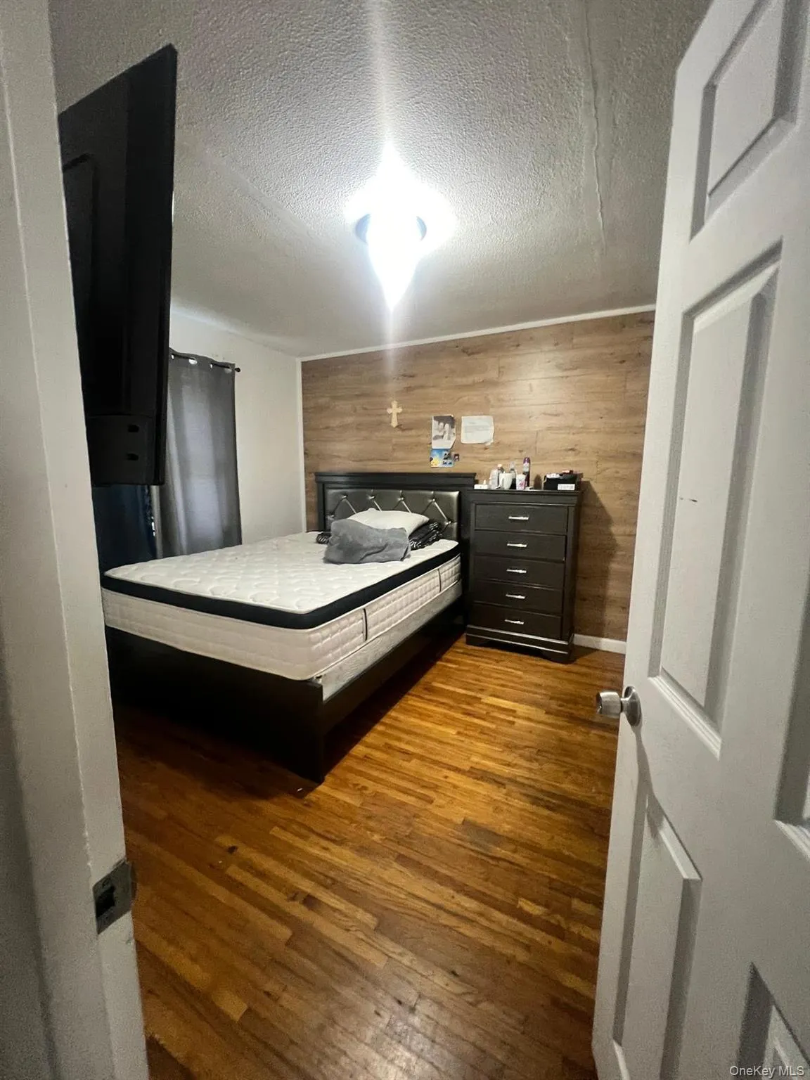 Bedroom featuring dark wood-style floors, wood walls, and a textured ceiling Bedroom featuring dark wood-style floors, wood walls, and a textured ceiling