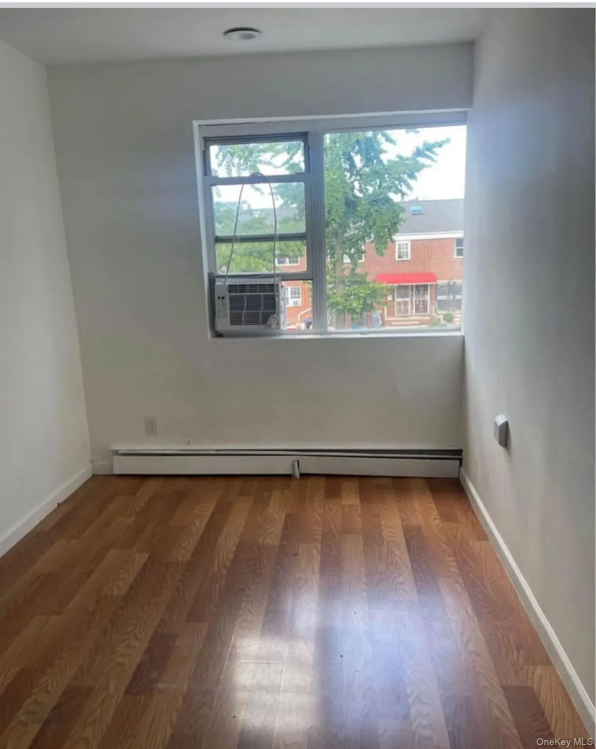 Unfurnished room with wood finished floors, a baseboard heating unit, and cooling unit Unfurnished room with wood finished floors, a baseboard heating unit, and cooling unit