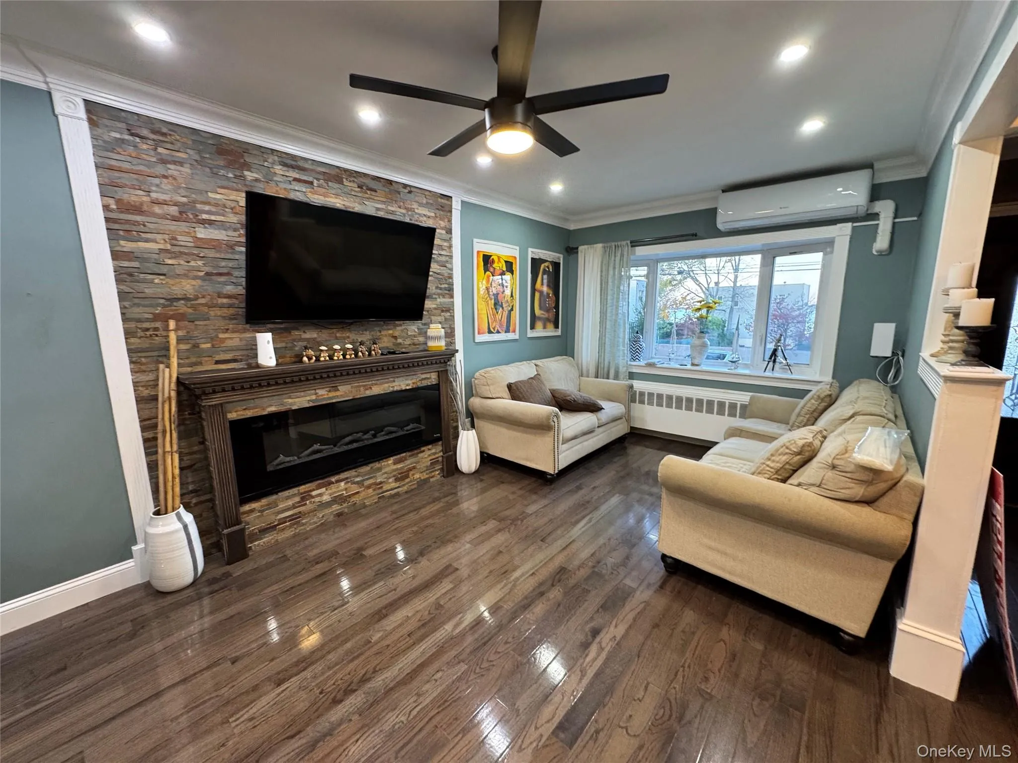 Living room with ornamental molding, a fireplace, dark wood-style flooring, radiator heating unit, and ceiling fan Living room with ornamental molding, a fireplace, dark wood-style flooring, radiator heating unit, and ceiling fan