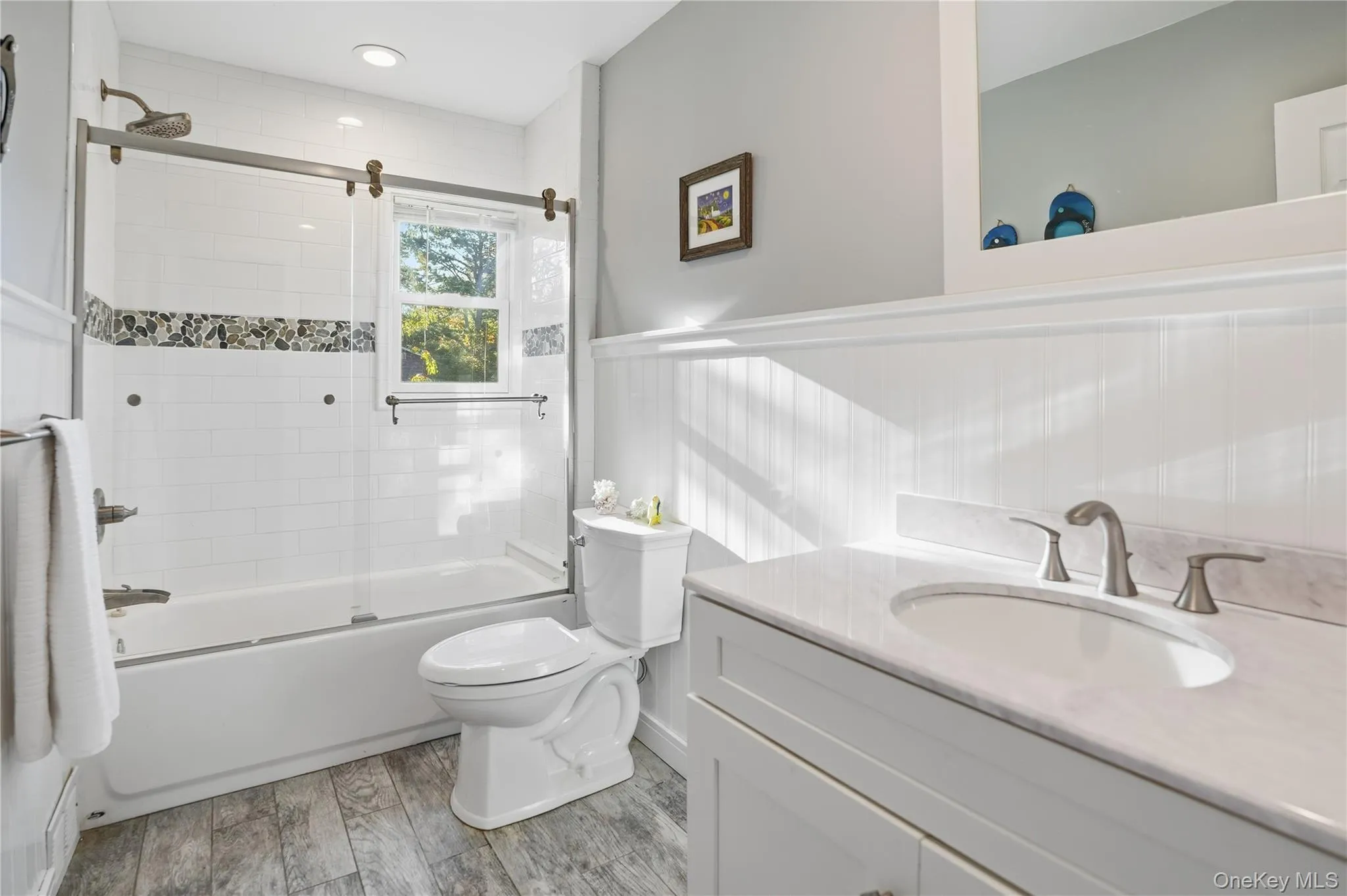 Full bath with vanity, combined bath / shower with glass door, and light wood-style floors Full bath with vanity, combined bath / shower with glass door, and light wood-style floors