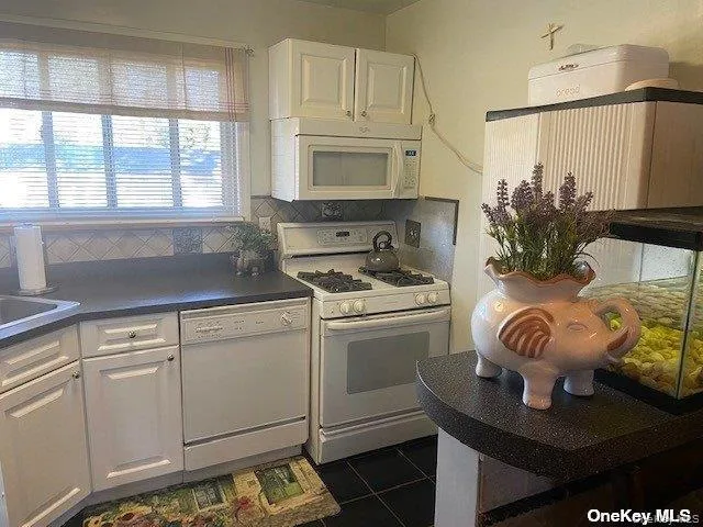 Kitchen with white cabinets, white appliances, dark countertops, tasteful backsplash, and dark tile patterned floors Kitchen with white cabinets, white appliances, dark countertops, tasteful backsplash, and dark tile patterned floors
