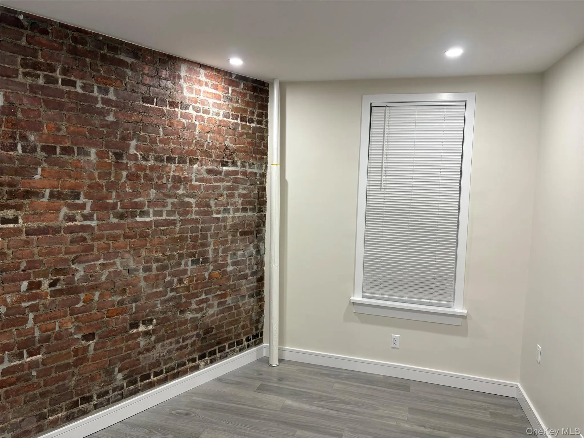 Unfurnished room featuring brick wall, wood finished floors, and recessed lighting Unfurnished room featuring brick wall, wood finished floors, and recessed lighting