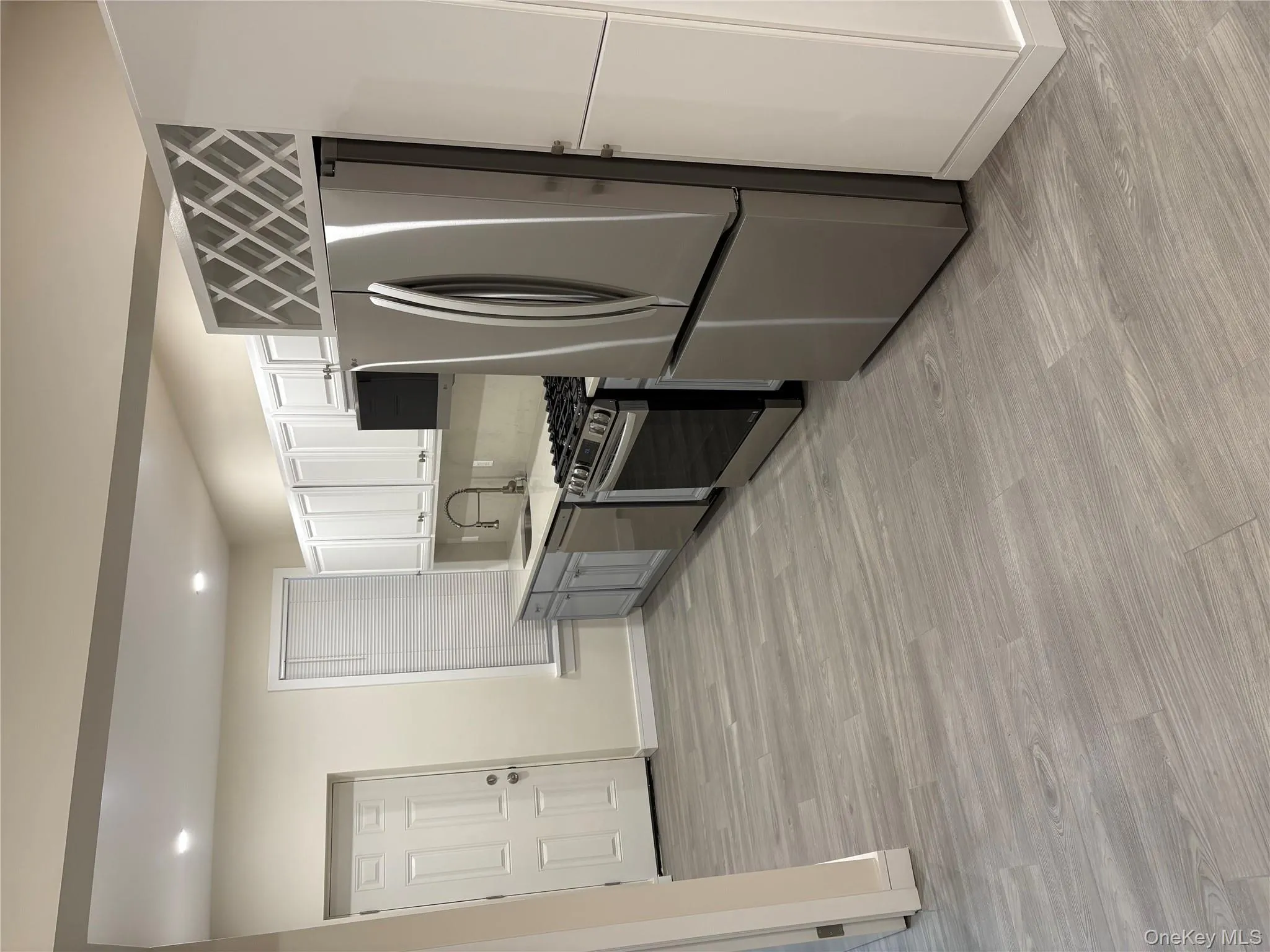 Kitchen with appliances with stainless steel finishes, white cabinets, recessed lighting, light wood-style flooring, and gray cabinetry Kitchen with appliances with stainless steel finishes, white cabinets, recessed lighting, light wood-style flooring, and gray cabinetry