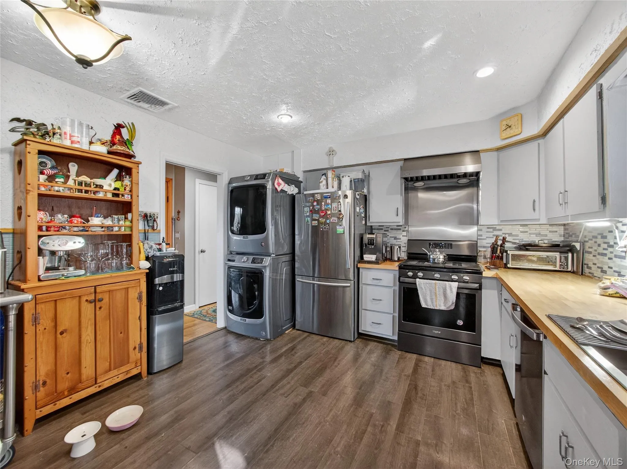 Kitchen with stainless steel appliances, decorative backsplash, dark wood-type flooring, stacked washer / dryer, and a textured ceiling Kitchen with stainless steel appliances, decorative backsplash, dark wood-type flooring, stacked washer / dryer, and a textured ceiling