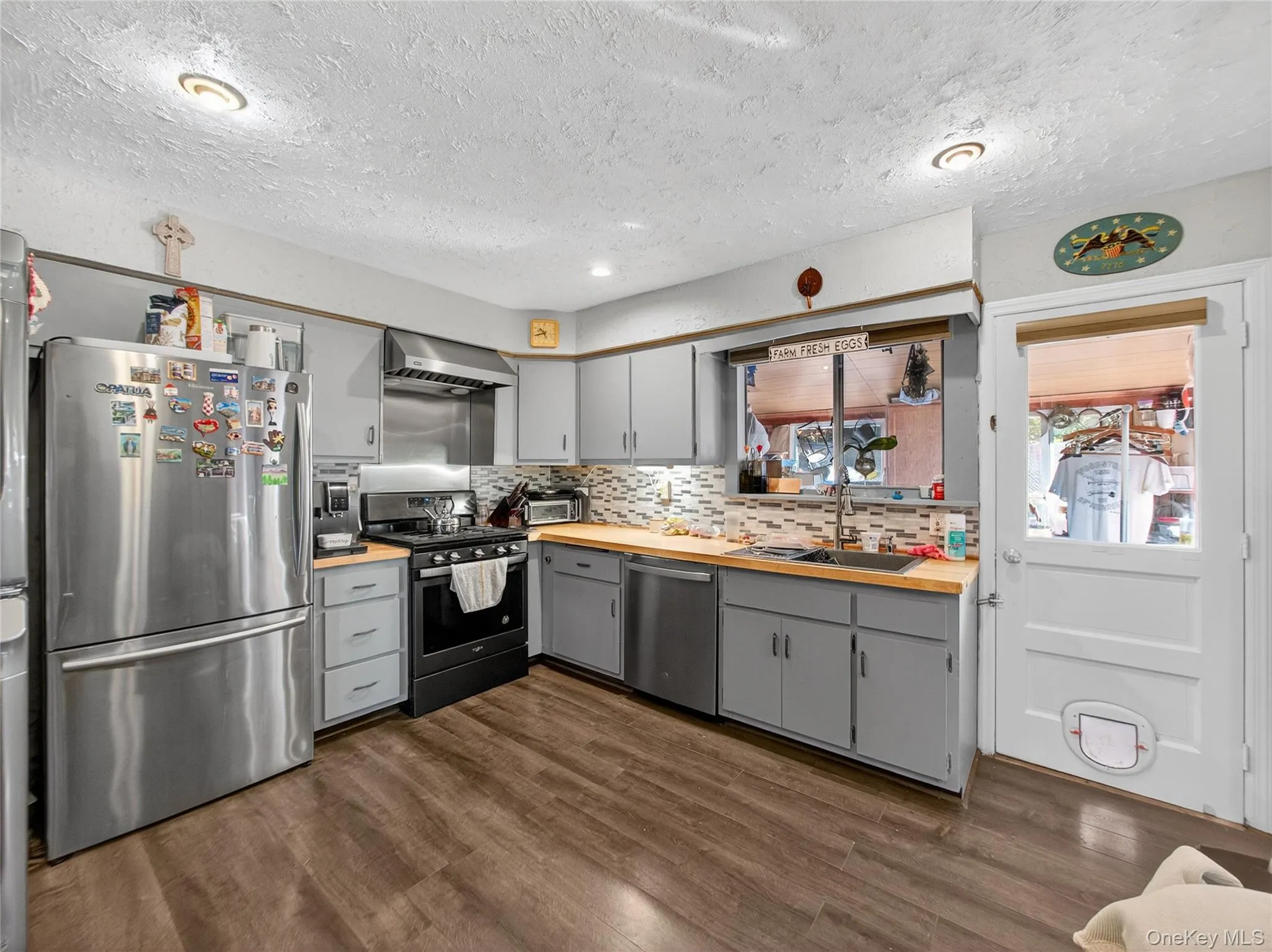 Kitchen with stainless steel appliances, decorative backsplash, dark wood finished floors, a textured ceiling, and gray cabinets Kitchen with stainless steel appliances, decorative backsplash, dark wood finished floors, a textured ceiling, and gray cabinets