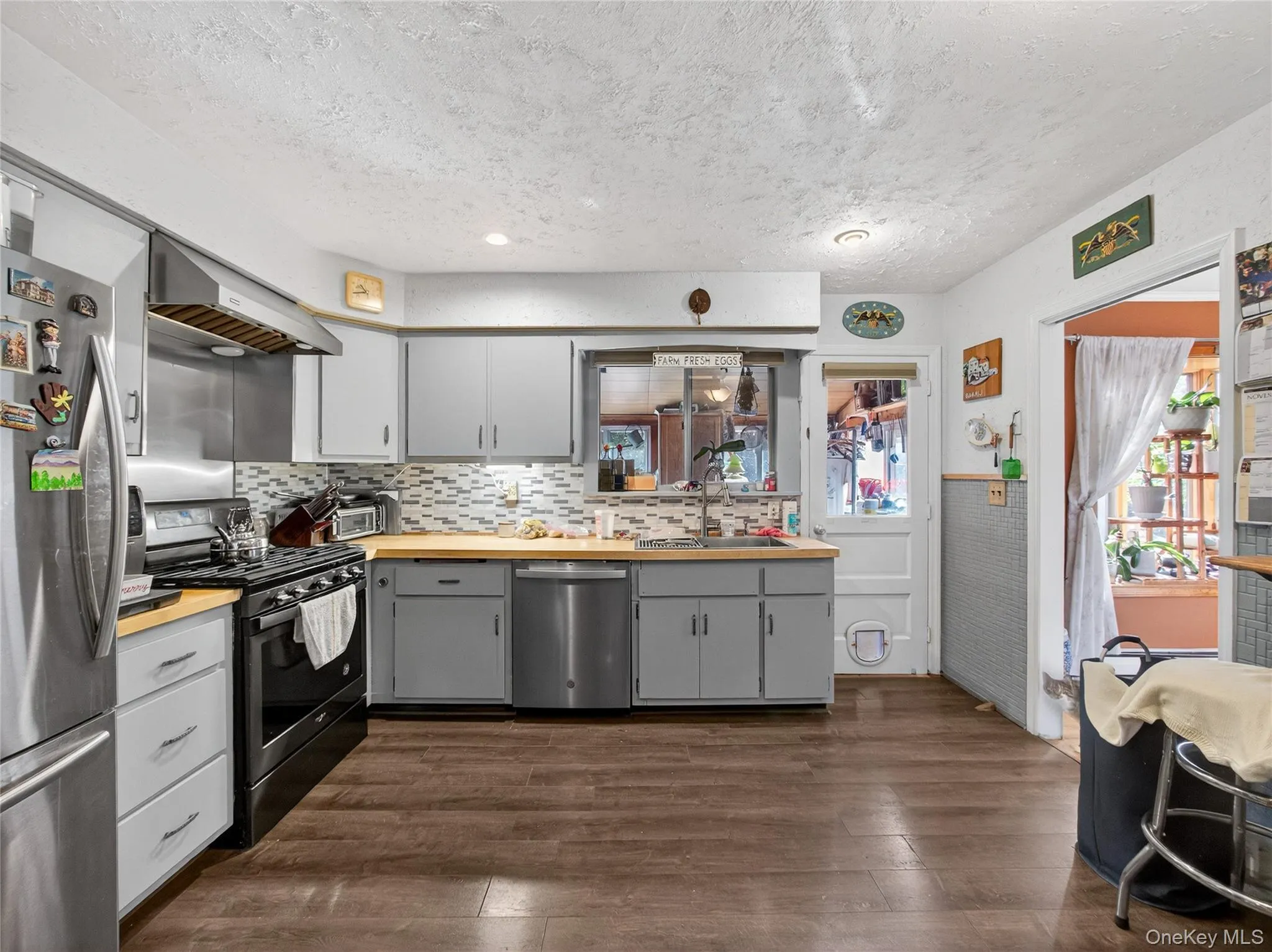 Kitchen featuring stainless steel appliances, dark wood-type flooring, range hood, backsplash, and wood counters Kitchen featuring stainless steel appliances, dark wood-type flooring, range hood, backsplash, and wood counters