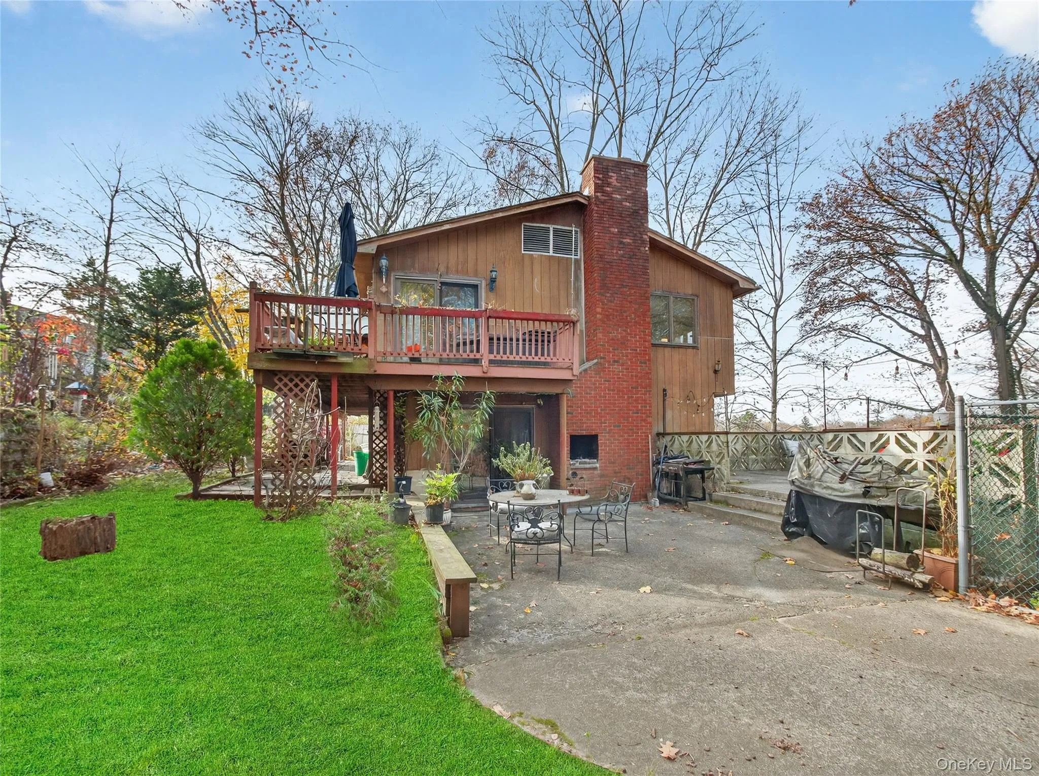 Rear view of house featuring a patio, a wooden deck, a lawn, and a chimney Rear view of house featuring a patio, a wooden deck, a lawn, and a chimney