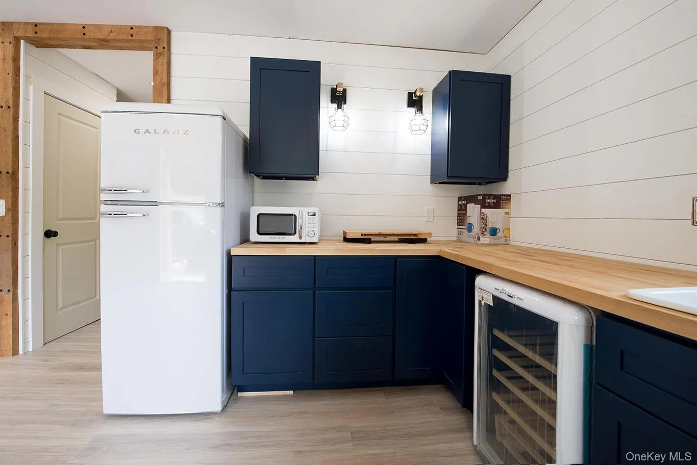 Kitchen with blue cabinets, beverage cooler, white appliances, and wooden walls Kitchen with blue cabinets, beverage cooler, white appliances, and wooden walls