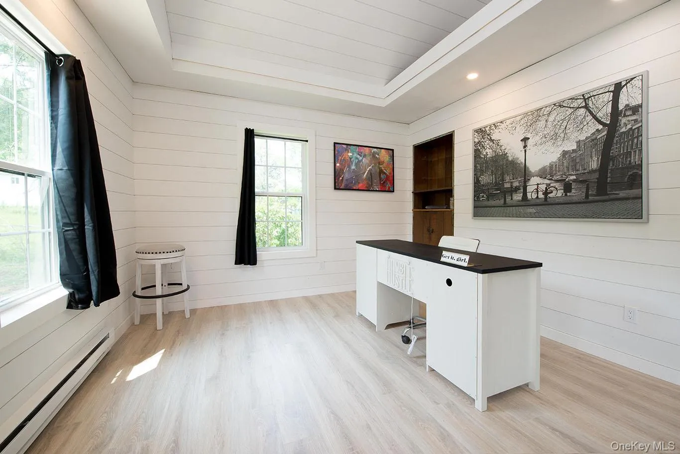 Unfurnished office with baseboard heating, a raised ceiling, light wood-type flooring, wooden walls, and recessed lighting Unfurnished office with baseboard heating, a raised ceiling, light wood-type flooring, wooden walls, and recessed lighting