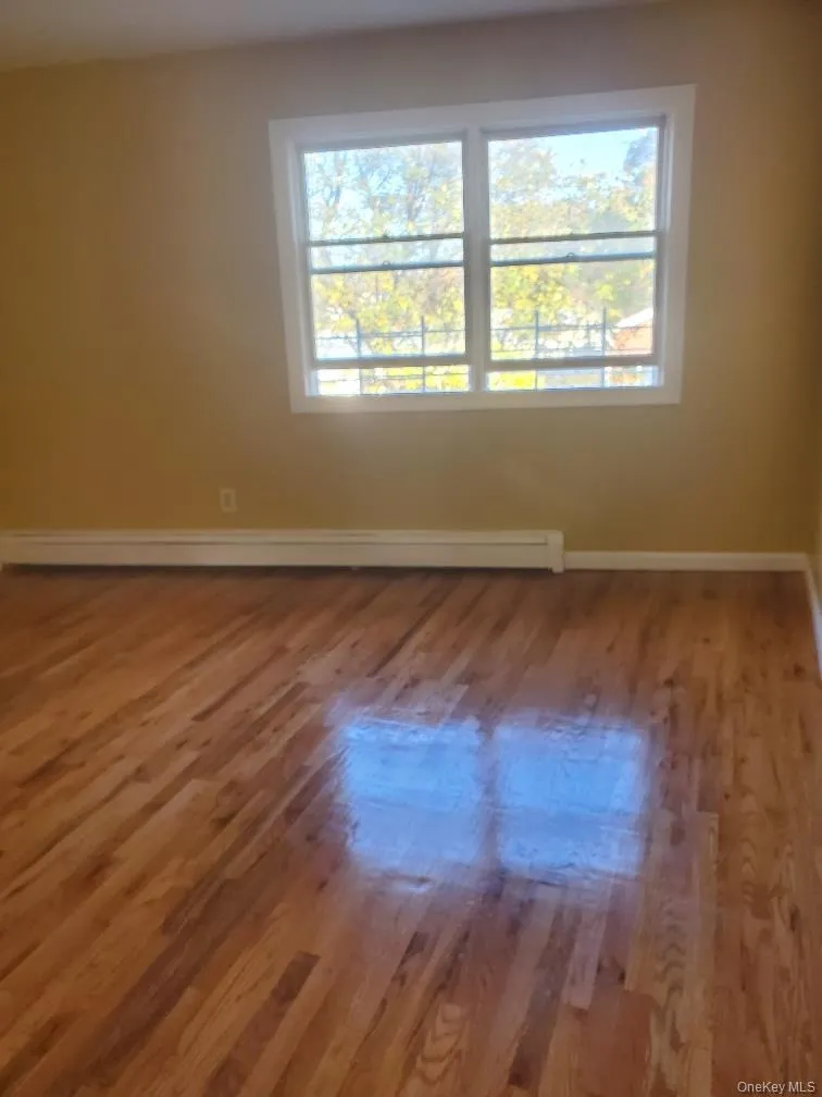 Empty room with healthy amount of natural light, wood finished floors, and a baseboard radiator Empty room with healthy amount of natural light, wood finished floors, and a baseboard radiator
