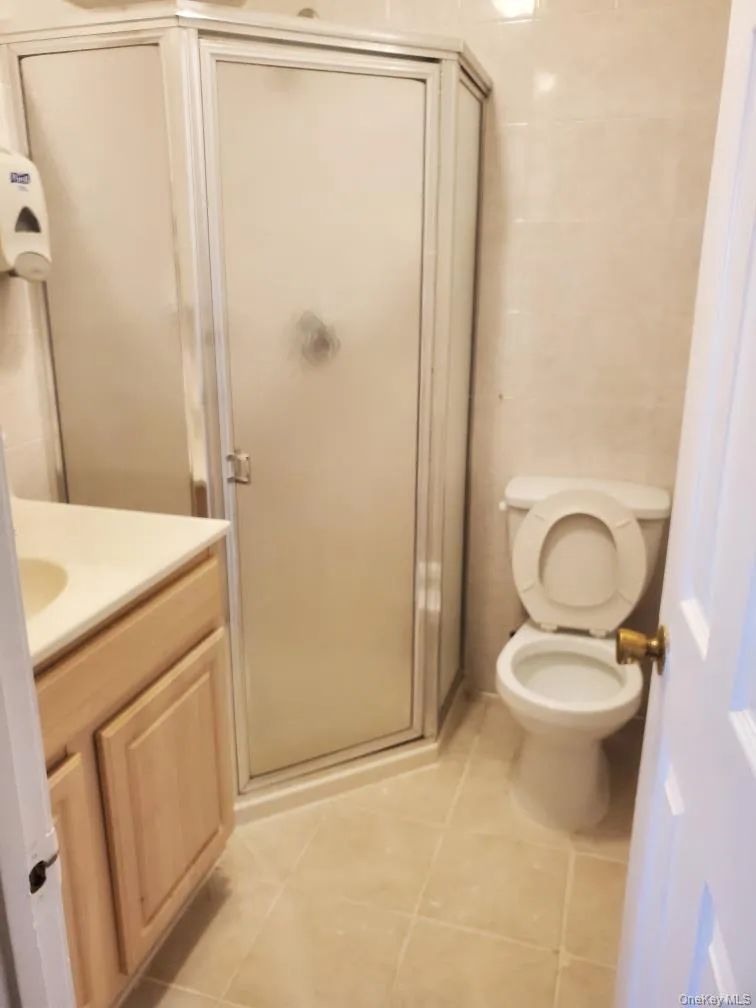 Bathroom with tile walls, vanity, a stall shower, and light tile patterned floors Bathroom with tile walls, vanity, a stall shower, and light tile patterned floors