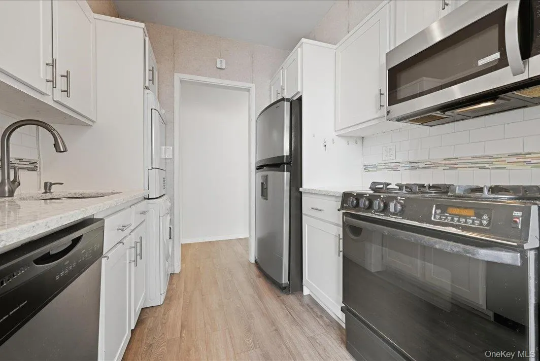 Kitchen featuring stainless steel appliances, white cabinets, light stone counters, and light wood-type flooring Kitchen featuring stainless steel appliances, white cabinets, light stone counters, and light wood-type flooring
