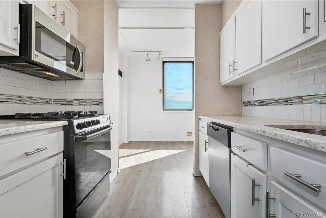 Kitchen with backsplash, stainless steel appliances, white cabinetry, light wood-style floors, and light stone counters Kitchen with backsplash, stainless steel appliances, white cabinetry, light wood-style floors, and light stone counters