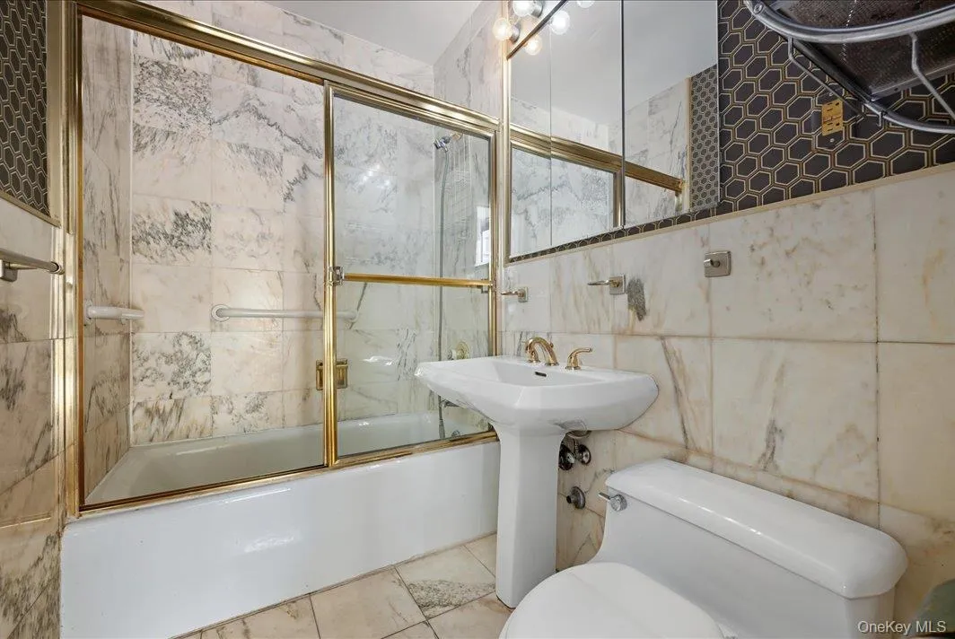 Full bath featuring tile walls and shower / bath combination with glass door Full bath featuring tile walls and shower / bath combination with glass door