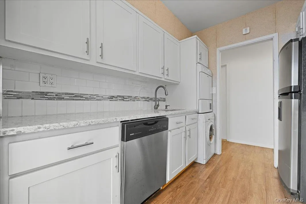 Kitchen featuring white cabinetry, appliances with stainless steel finishes, light wood-style flooring, light stone countertops, and stacked washer / drying machine Kitchen featuring white cabinetry, appliances with stainless steel finishes, light wood-style flooring, light stone countertops, and stacked washer / drying machine